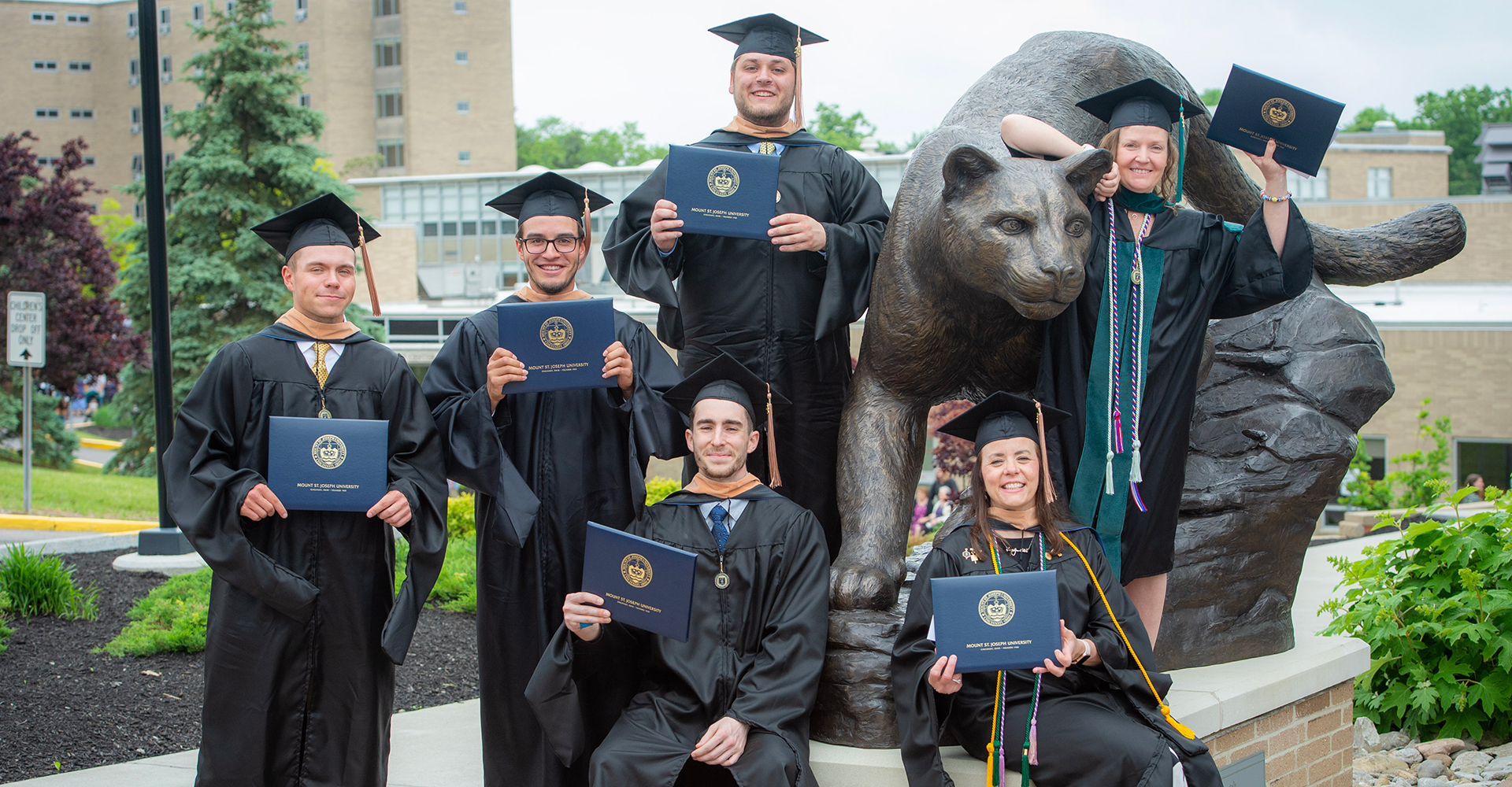 graduates standing by lions statue with diplomas