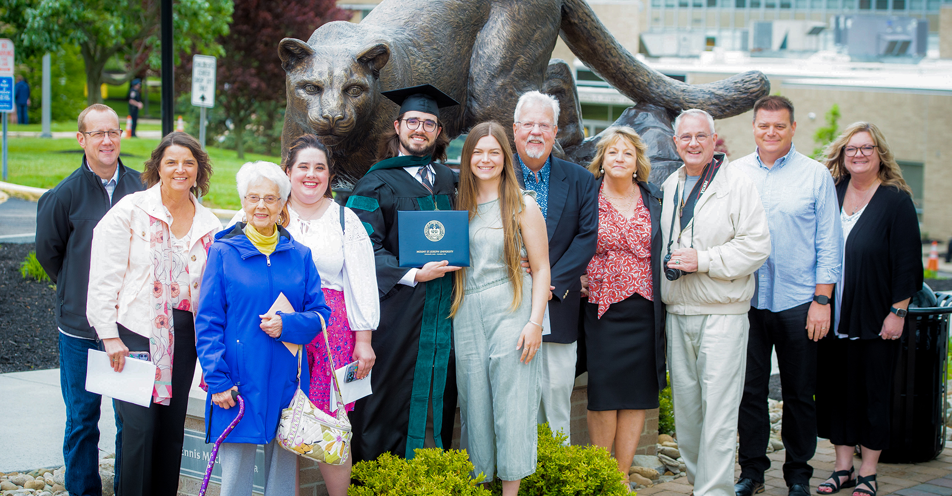 graduates standing by lions statue with diplomas