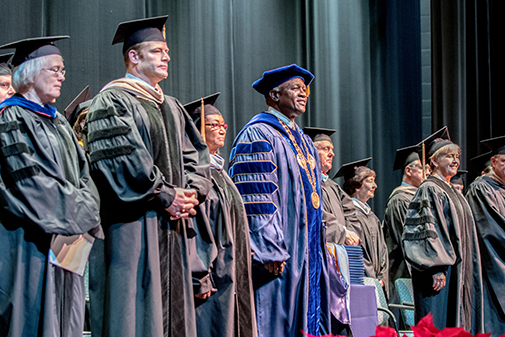 Faculty and President Williams standing on stage in regalia for commencement.